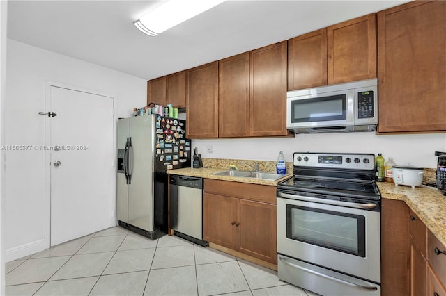 kitchen featuring light stone countertops, appliances with stainless steel finishes, light tile floors, and sink