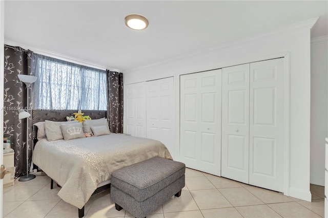 bedroom with crown molding, light tile flooring, and two closets