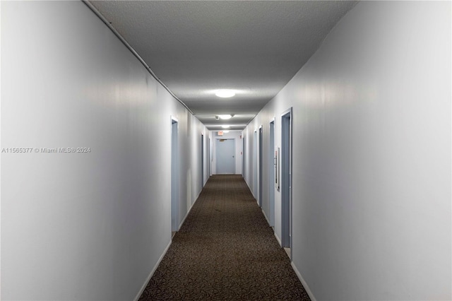 hallway featuring a textured ceiling and dark carpet