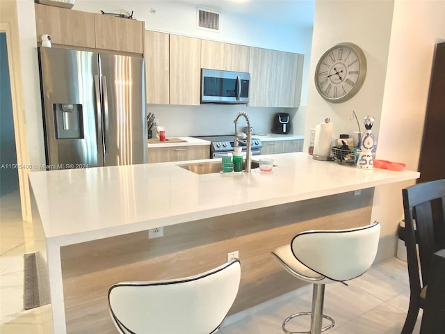 kitchen featuring kitchen peninsula, a breakfast bar, appliances with stainless steel finishes, and sink