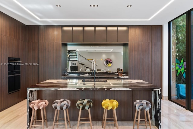 kitchen with dark brown cabinetry, dark countertops, modern cabinets, a kitchen breakfast bar, and a sink