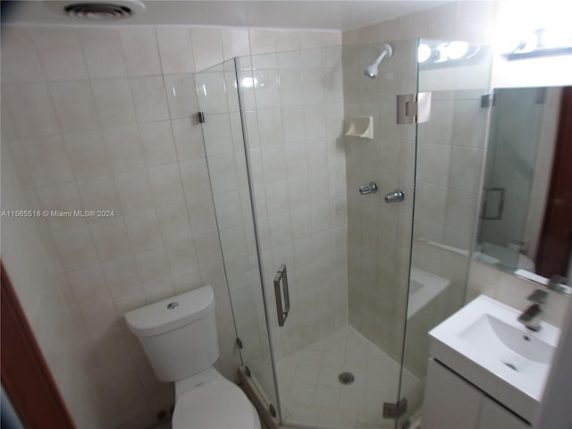 bathroom featuring vanity, a shower with shower door, tile walls, and toilet