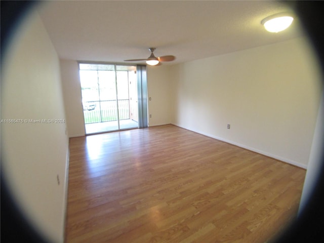 unfurnished room with ceiling fan, a wall of windows, and light hardwood / wood-style flooring