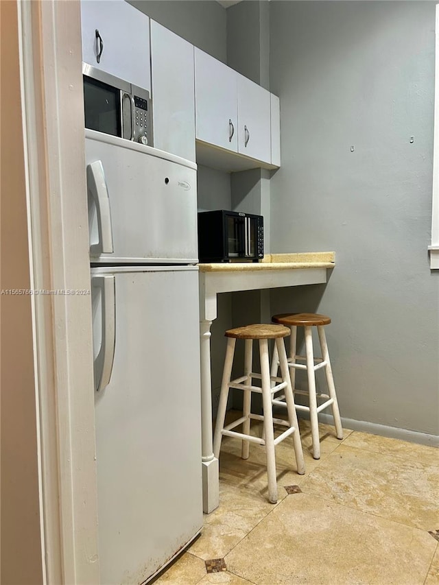 kitchen with white cabinets, a kitchen breakfast bar, and white fridge