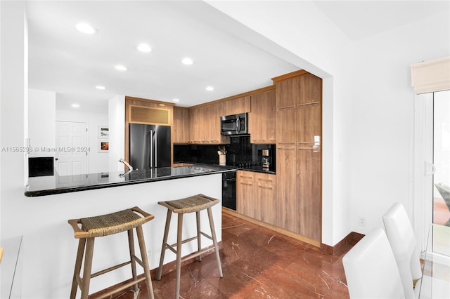 kitchen featuring dark stone countertops, tasteful backsplash, a kitchen bar, kitchen peninsula, and appliances with stainless steel finishes