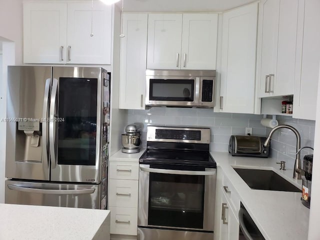 kitchen with light stone counters, tasteful backsplash, white cabinetry, stainless steel appliances, and sink