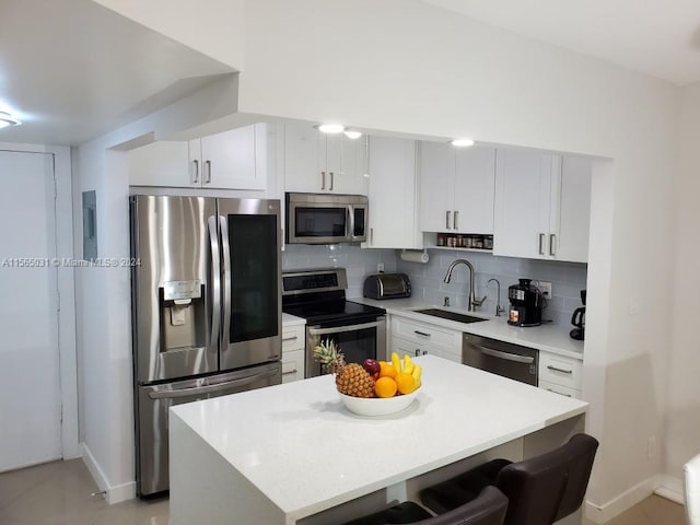 kitchen with stainless steel appliances, a kitchen breakfast bar, white cabinetry, backsplash, and sink