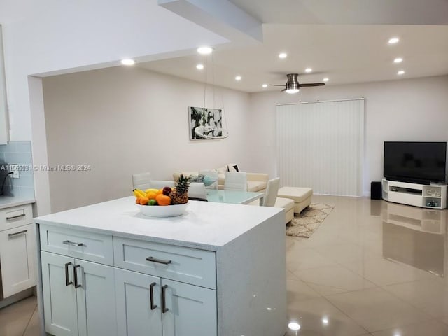 kitchen featuring pendant lighting, a kitchen island, light tile floors, ceiling fan, and white cabinets