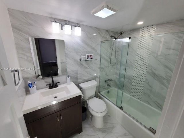 full bathroom featuring toilet, vanity with extensive cabinet space, tile walls, combined bath / shower with glass door, and tile floors