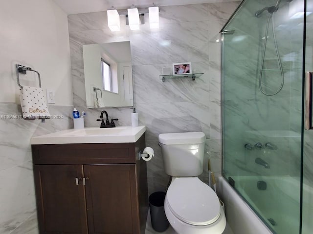 full bathroom with bath / shower combo with glass door, tile walls, toilet, and vanity