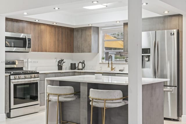 kitchen with appliances with stainless steel finishes, light stone counters, a breakfast bar area, a raised ceiling, and sink