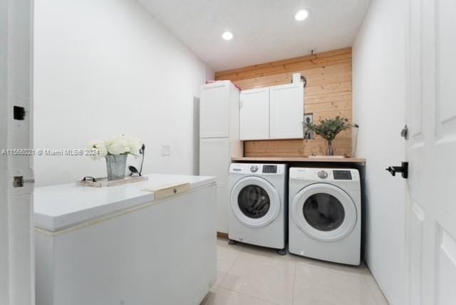 laundry room with washing machine and clothes dryer, wood walls, light tile patterned flooring, and cabinets