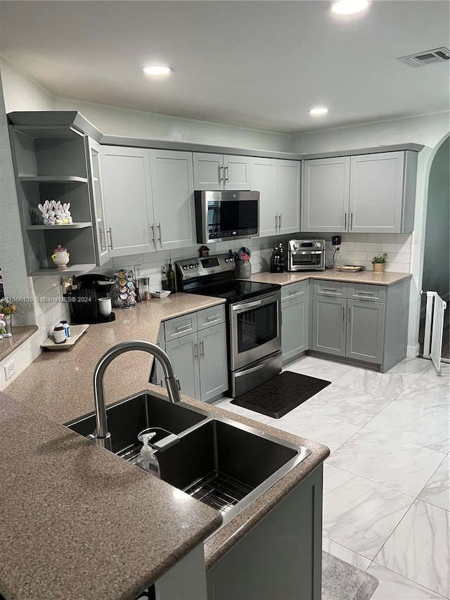 kitchen with stainless steel appliances, gray cabinets, backsplash, sink, and light tile floors