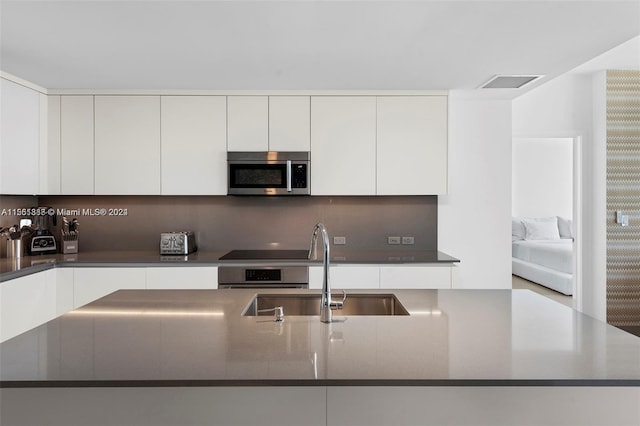 kitchen featuring dark stone counters, white cabinets, backsplash, electric stovetop, and sink