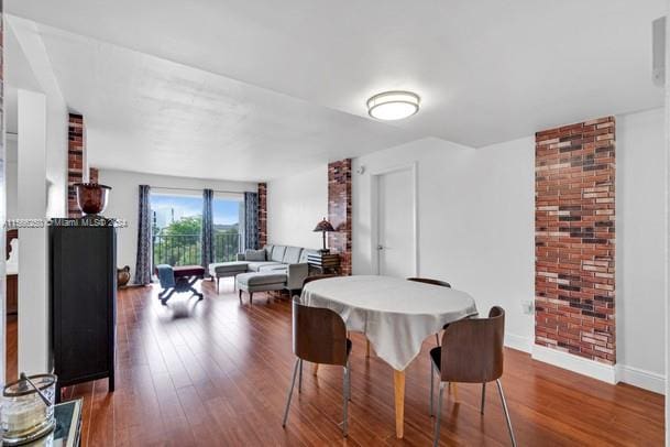 dining space with brick wall and dark wood-type flooring