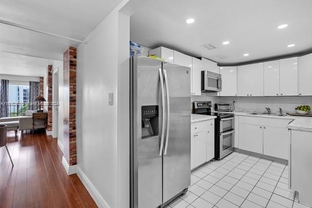 kitchen featuring tasteful backsplash, white cabinets, stainless steel appliances, sink, and light tile flooring