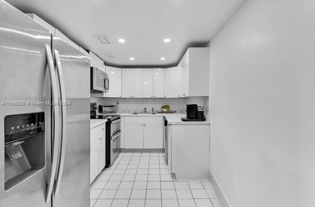 kitchen featuring sink, appliances with stainless steel finishes, white cabinetry, and light tile flooring