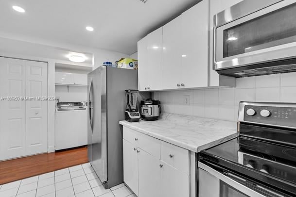 kitchen with stainless steel appliances, washer / dryer, white cabinets, backsplash, and light wood-type flooring