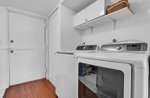 laundry room featuring dark hardwood / wood-style flooring, washing machine and clothes dryer, and cabinets