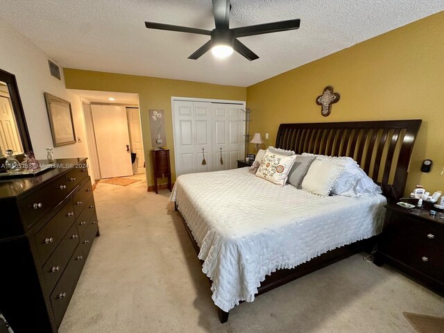 bedroom featuring light carpet, ceiling fan, two closets, and a textured ceiling