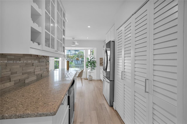 kitchen with white cabinetry, stainless steel appliances, light stone counters, tasteful backsplash, and light hardwood / wood-style floors