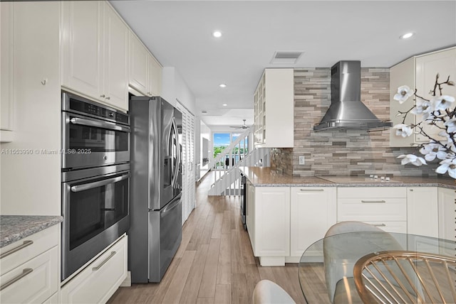 kitchen featuring white cabinetry, stainless steel appliances, light stone counters, decorative backsplash, and wall chimney exhaust hood