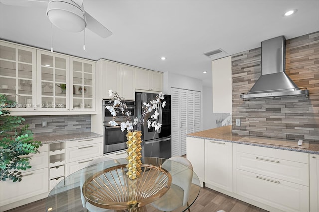 kitchen with white cabinets, appliances with stainless steel finishes, light stone countertops, and wall chimney range hood