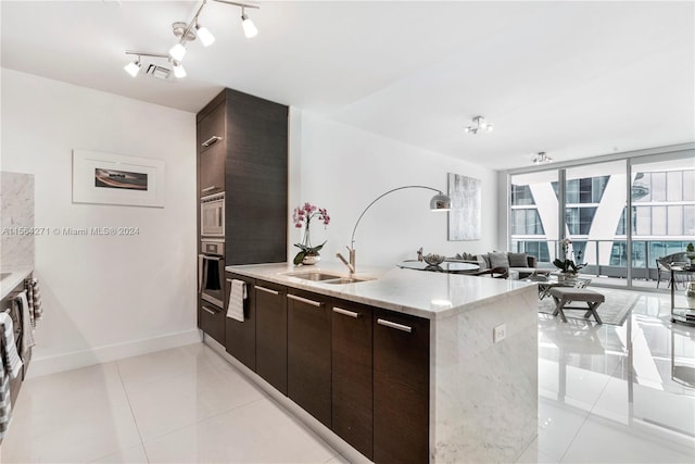 kitchen with dark brown cabinetry, rail lighting, light tile patterned flooring, and stainless steel appliances