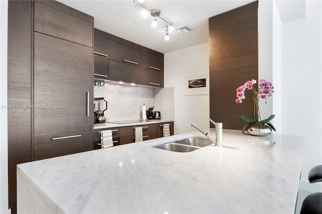 kitchen with black electric cooktop, decorative backsplash, sink, light stone counters, and track lighting