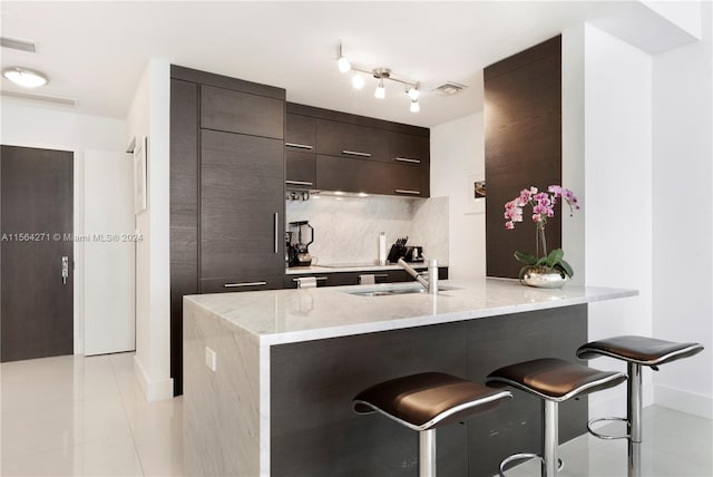 kitchen with kitchen peninsula, backsplash, light stone countertops, light tile patterned floors, and a kitchen breakfast bar