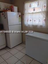 kitchen with white refrigerator, white cabinetry, and light tile floors