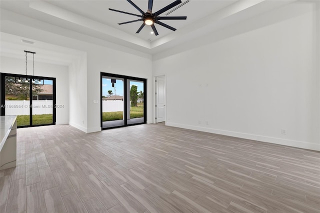 spare room with a tray ceiling, light wood-type flooring, and ceiling fan