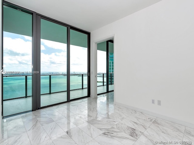 tiled empty room with a water view, a wealth of natural light, and a wall of windows