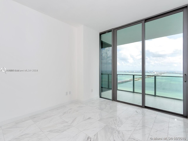 empty room featuring a water view, expansive windows, and light tile floors