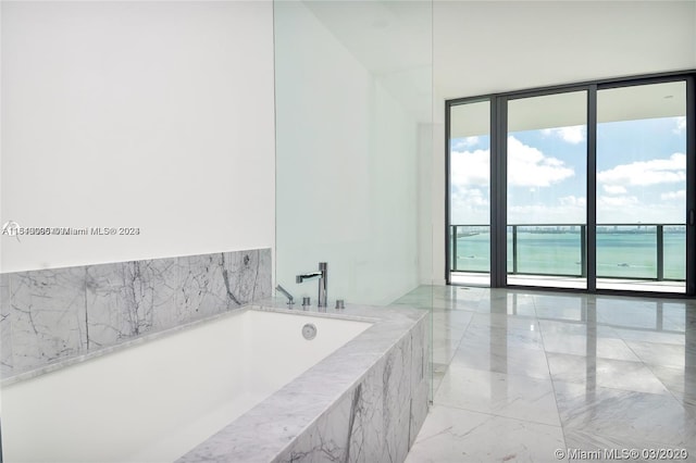 bathroom featuring tile flooring, a water view, a wealth of natural light, and tiled bath