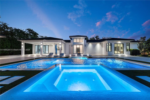 pool at dusk featuring a patio, an in ground hot tub, pool water feature, and french doors