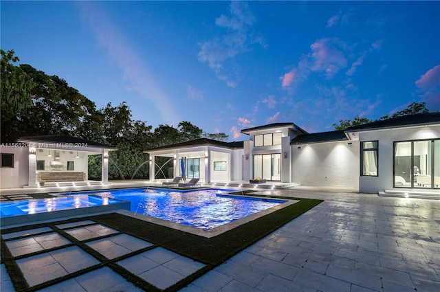 pool at dusk with a patio, a jacuzzi, area for grilling, exterior bar, and pool water feature