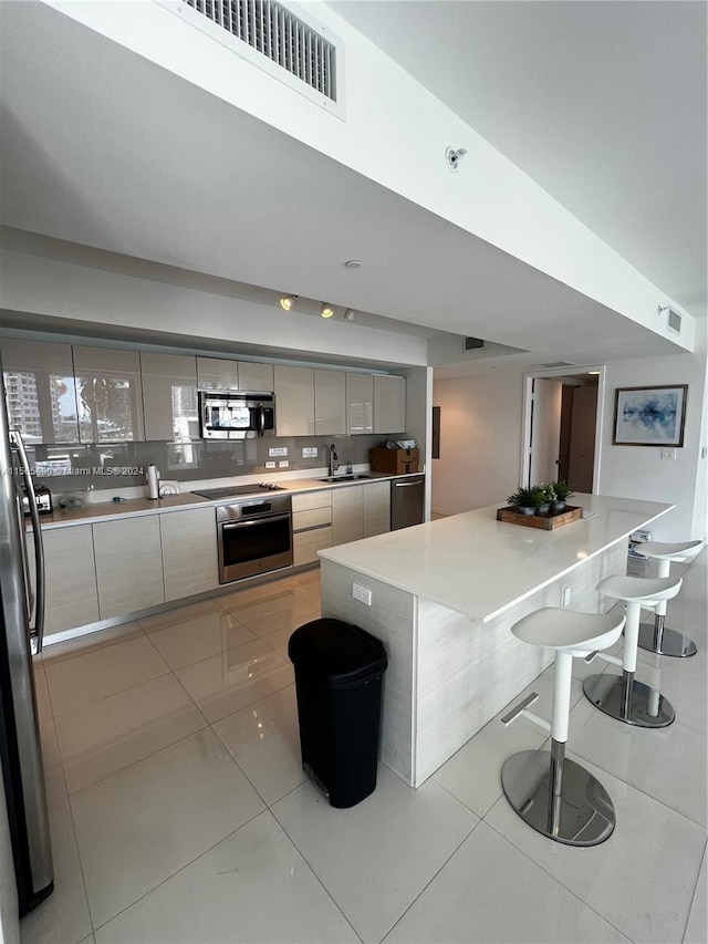 kitchen with sink, gray cabinets, a breakfast bar, stainless steel appliances, and light tile flooring