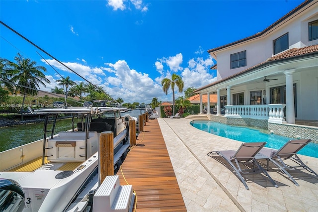 view of swimming pool featuring a patio area, a boat dock, ceiling fan, and a water view