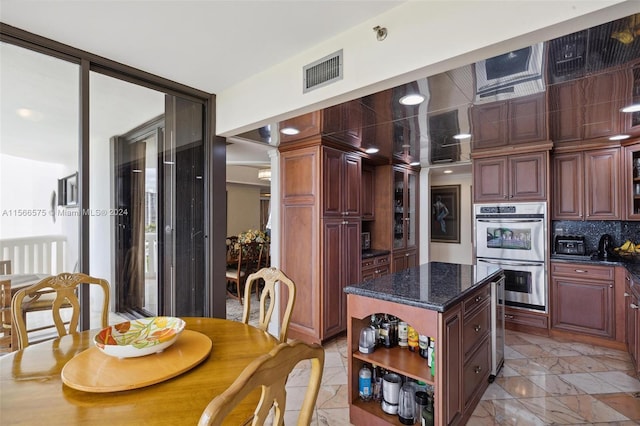 kitchen featuring double oven, decorative backsplash, a center island, and dark stone counters