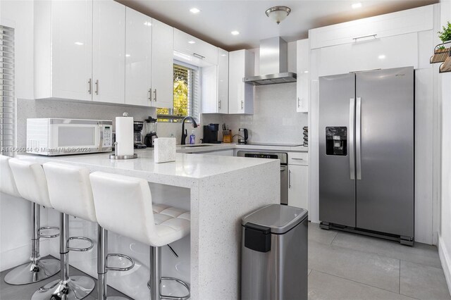 kitchen featuring sink, white cabinetry, kitchen peninsula, wall chimney exhaust hood, and stainless steel appliances