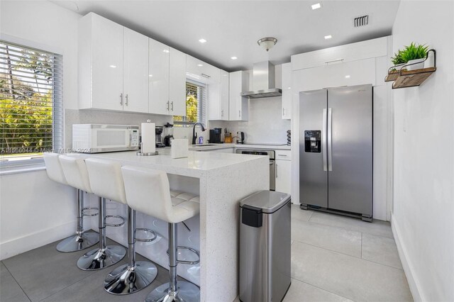 kitchen featuring white cabinets, wall chimney exhaust hood, light stone countertops, light tile patterned floors, and stainless steel appliances