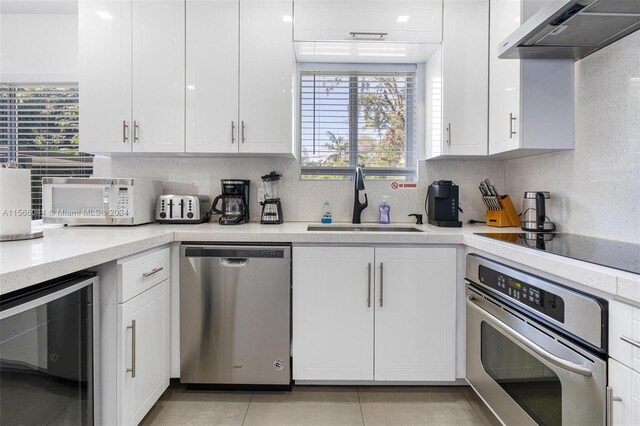 kitchen with exhaust hood, wine cooler, appliances with stainless steel finishes, and white cabinets