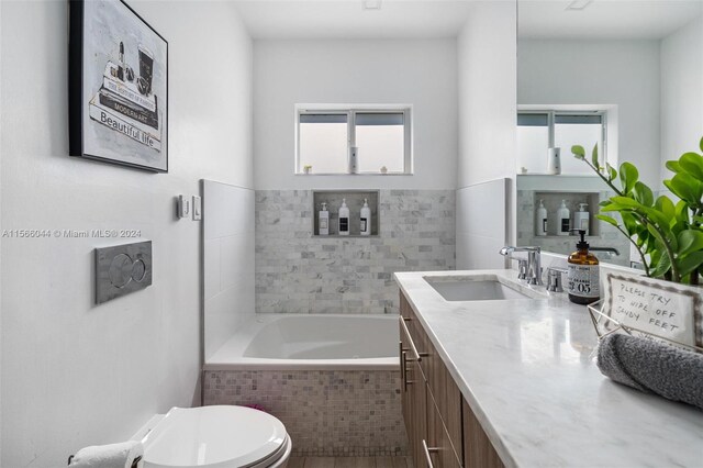 bathroom with tiled bath, vanity, toilet, and plenty of natural light