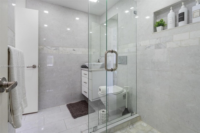 bathroom with tile walls, a shower with shower door, vanity, toilet, and tile patterned floors