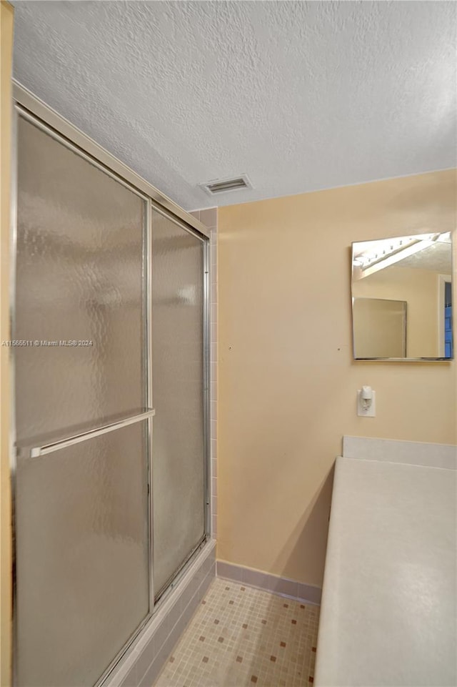 bathroom with a shower with door, a textured ceiling, and tile floors