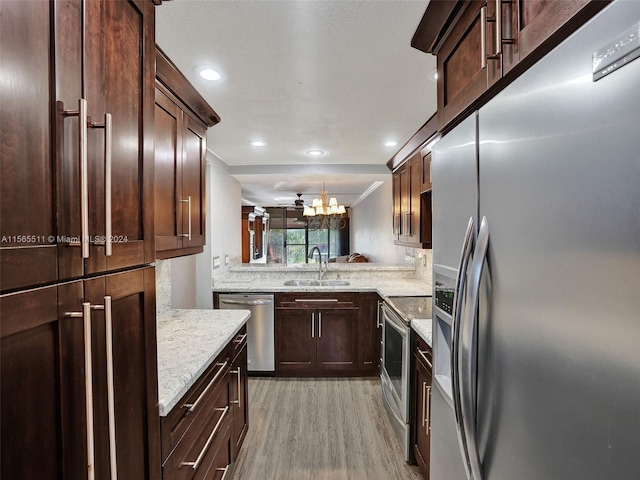 kitchen featuring an inviting chandelier, light stone counters, stainless steel appliances, light wood-type flooring, and sink