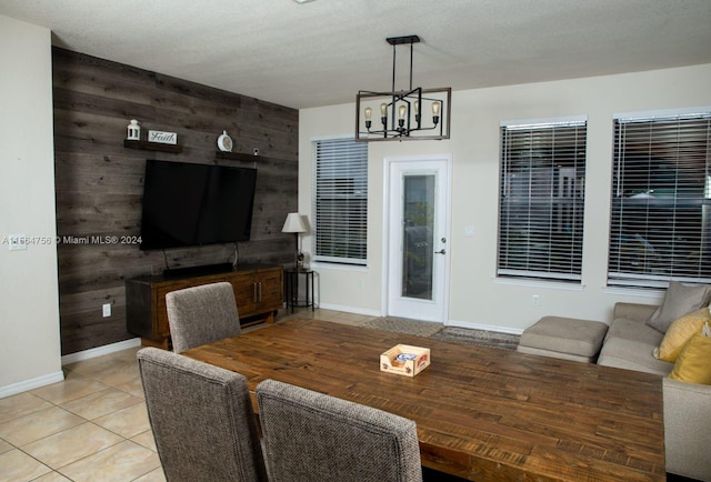 dining room featuring a notable chandelier, wood walls, a textured ceiling, and light tile flooring