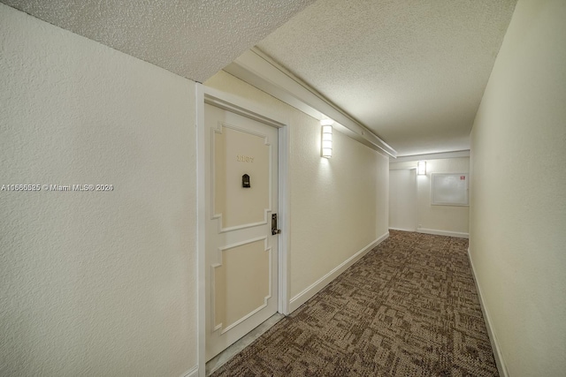 hall featuring a textured ceiling and dark colored carpet