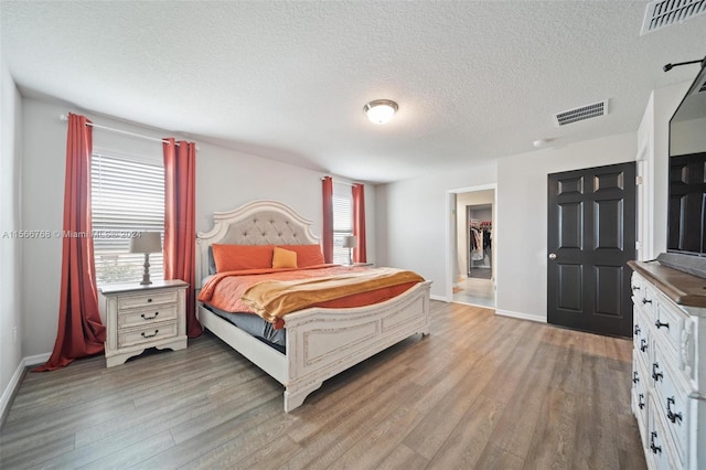 bedroom with a textured ceiling, a closet, light hardwood / wood-style floors, and a spacious closet